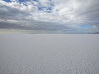 two people skiing on an icy and empty surface with clouds in the sky on the horizon