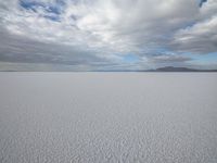 two people skiing on an icy and empty surface with clouds in the sky on the horizon