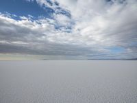 two people skiing on an icy and empty surface with clouds in the sky on the horizon