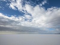 two people skiing on an icy and empty surface with clouds in the sky on the horizon