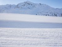 two people riding skis on snow covered ground next to mountains side by side,