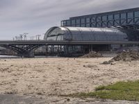 two people walk across the street past buildings and a bridge in front of them and some dirt