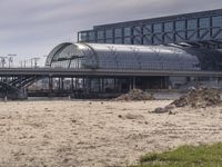 two people walk across the street past buildings and a bridge in front of them and some dirt