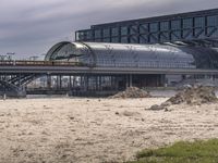 two people walk across the street past buildings and a bridge in front of them and some dirt