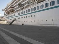 two people walk down an empty sidewalk by a large cruise ship, with stairs to the back and the front