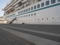 two people walk down an empty sidewalk by a large cruise ship, with stairs to the back and the front