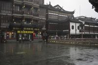 two people walking in the rain on a city street near a building with two towers