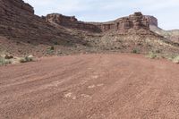 two vehicles are traveling along a dirt road in the mountains at daytime time and red rock formation