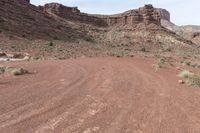 two vehicles are traveling along a dirt road in the mountains at daytime time and red rock formation