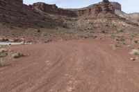 two vehicles are traveling along a dirt road in the mountains at daytime time and red rock formation