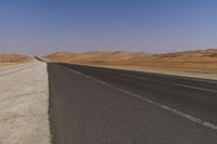 an empty road near a sandy desert and a few hills in the background with no one on it