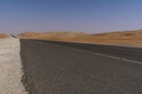 an empty road near a sandy desert and a few hills in the background with no one on it