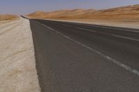 an empty road near a sandy desert and a few hills in the background with no one on it