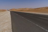 an empty road near a sandy desert and a few hills in the background with no one on it