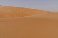 a lone man is walking through the desert dunes with a large sand dune behind him