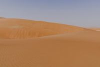 a lone man is walking through the desert dunes with a large sand dune behind him