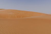 a lone man is walking through the desert dunes with a large sand dune behind him