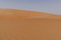 a lone man is walking through the desert dunes with a large sand dune behind him