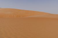 a lone man is walking through the desert dunes with a large sand dune behind him