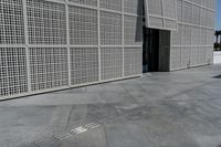a white building with many holes in the side and on the sidewalk behind it is an open door