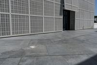 a white building with many holes in the side and on the sidewalk behind it is an open door