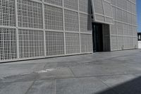 a white building with many holes in the side and on the sidewalk behind it is an open door