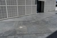 a white building with many holes in the side and on the sidewalk behind it is an open door