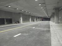 a street with white lines in an underground parking garage area at night, with a red traffic light on and overhead lighting in the ceiling