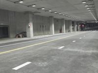 a street with white lines in an underground parking garage area at night, with a red traffic light on and overhead lighting in the ceiling
