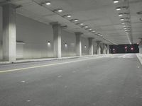 a street with white lines in an underground parking garage area at night, with a red traffic light on and overhead lighting in the ceiling