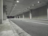 a street with white lines in an underground parking garage area at night, with a red traffic light on and overhead lighting in the ceiling