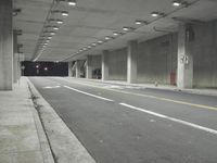 a street with white lines in an underground parking garage area at night, with a red traffic light on and overhead lighting in the ceiling