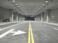 a street with white lines in an underground parking garage area at night, with a red traffic light on and overhead lighting in the ceiling