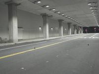 a street with white lines in an underground parking garage area at night, with a red traffic light on and overhead lighting in the ceiling