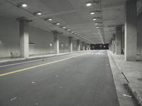 a street with white lines in an underground parking garage area at night, with a red traffic light on and overhead lighting in the ceiling