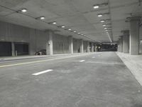 a street with white lines in an underground parking garage area at night, with a red traffic light on and overhead lighting in the ceiling
