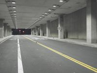 a street with white lines in an underground parking garage area at night, with a red traffic light on and overhead lighting in the ceiling