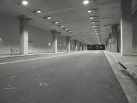 a street with white lines in an underground parking garage area at night, with a red traffic light on and overhead lighting in the ceiling