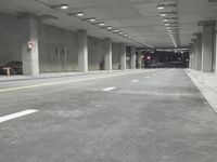 a street with white lines in an underground parking garage area at night, with a red traffic light on and overhead lighting in the ceiling