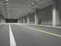a street with white lines in an underground parking garage area at night, with a red traffic light on and overhead lighting in the ceiling