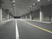 a street with white lines in an underground parking garage area at night, with a red traffic light on and overhead lighting in the ceiling