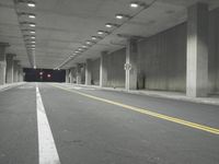 a street with white lines in an underground parking garage area at night, with a red traffic light on and overhead lighting in the ceiling