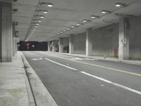 a street with white lines in an underground parking garage area at night, with a red traffic light on and overhead lighting in the ceiling