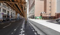 the view down the street from underneath the train tracks on a city street lined with buildings and cars