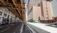 the view down the street from underneath the train tracks on a city street lined with buildings and cars