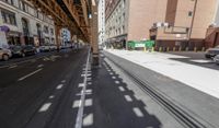 the view down the street from underneath the train tracks on a city street lined with buildings and cars