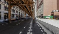 the view down the street from underneath the train tracks on a city street lined with buildings and cars