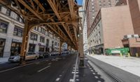 the view down the street from underneath the train tracks on a city street lined with buildings and cars