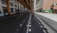 the view down the street from underneath the train tracks on a city street lined with buildings and cars