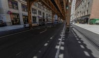 the view down the street from underneath the train tracks on a city street lined with buildings and cars